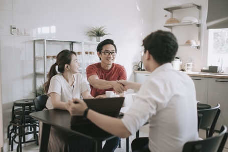Young couple sits with an insurance broker at a table in a well-lit kitchen