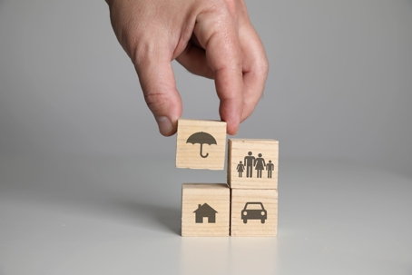 Hand lifting a wooden block with an umbrella on it as it is stacked with other blocks with pictures on them, representing insurance