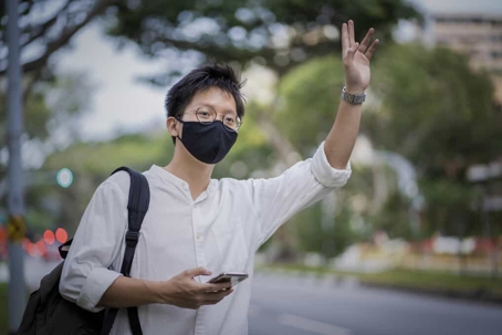 Man wearing a black face mask hails a ride on the street