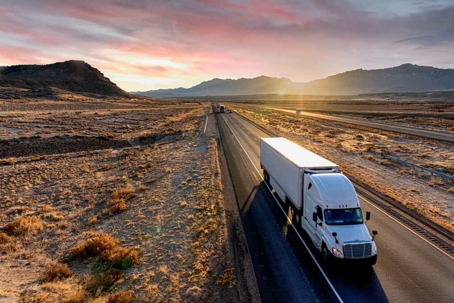 Large commercial truck drives down a lonely two-lane highway in the desert