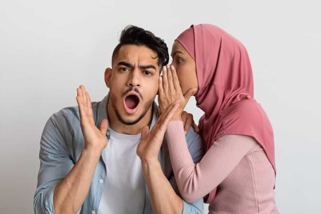 Young woman wearing a hijab tells a young man a shocking secret