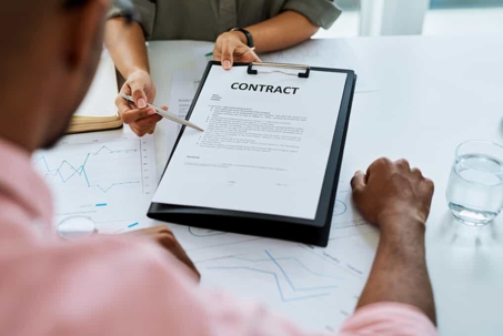 Close up of a woman's hands presenting a contract to a man over a white table with a glass of water sitting on it