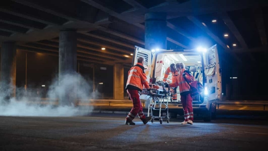 Emergency medical personnel rush an injured victim on a gurney into an ambulance at night
