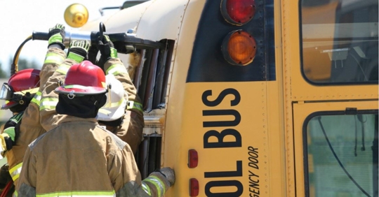 School bus on it's side, firefighters surrounding the vehicle