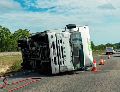 Truck lays on its side on a highway after a rollover truck accident on a partly cloudy day